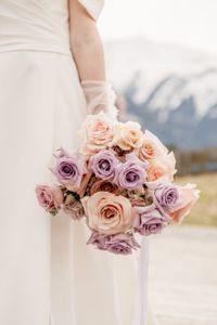 Braut in den Bergen mit Brautstrauss aus verschiedenen pastellfarbenen Rosen